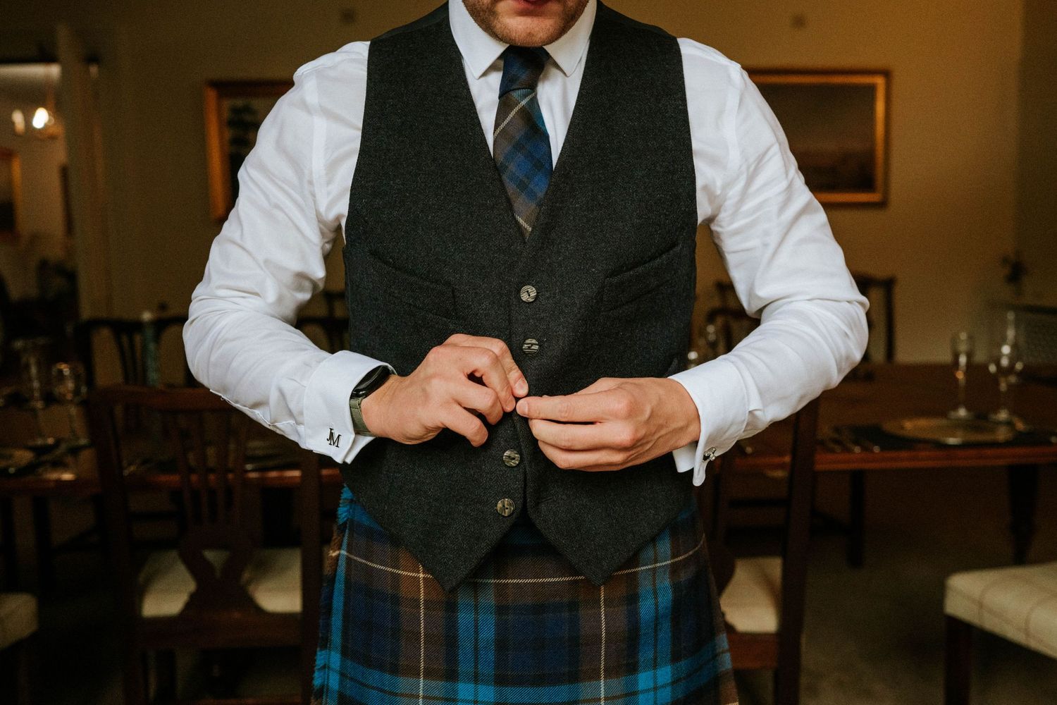 Men in formal Scottish attire adjusting traditional kilt accessories and clothing.