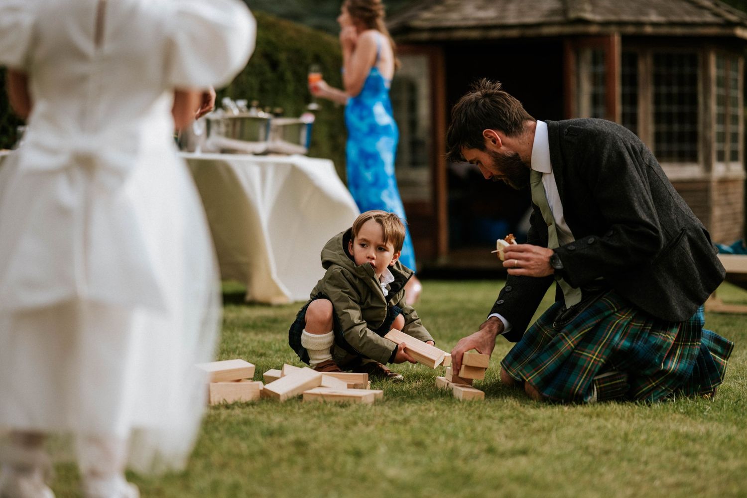 A heartwarming moment at a wedding as guests interact on the lawn near a garden structure.
