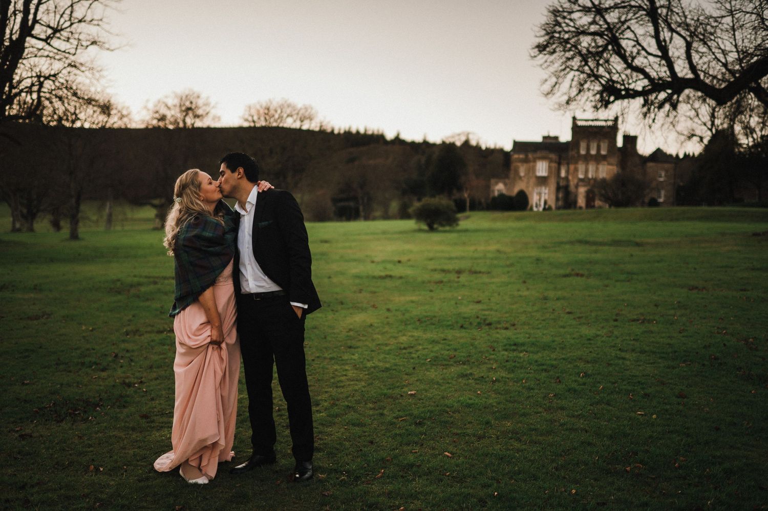 A romantic silhouette of a couple embracing in a field with a mansion in the distance.