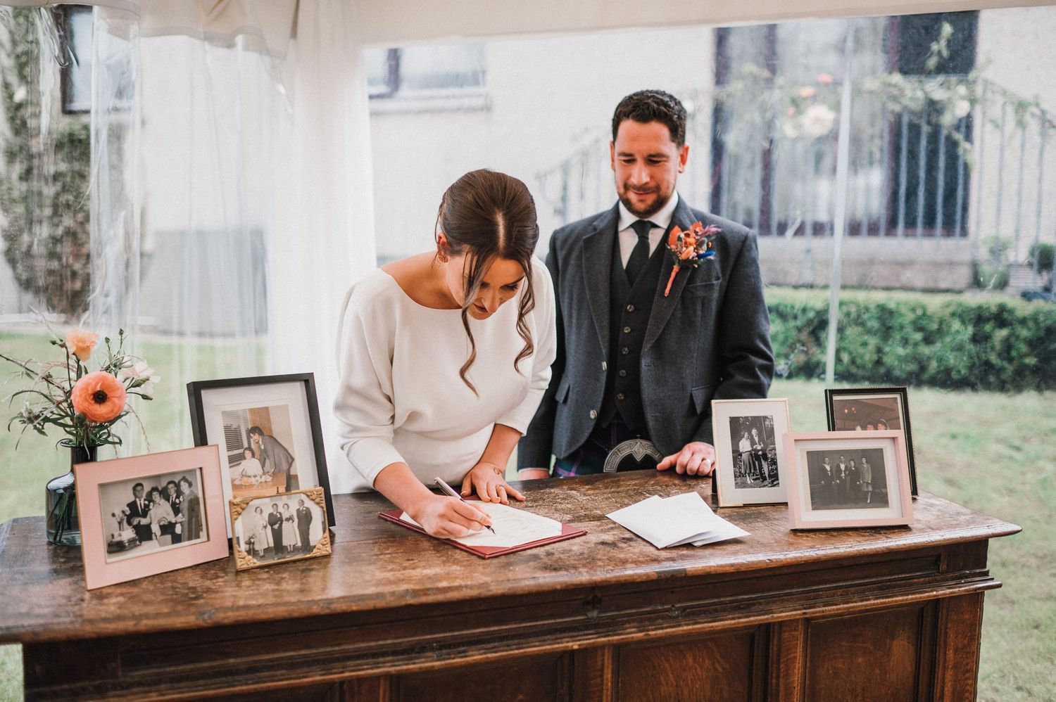 Wedding ceremony signing moment at rustic wooden table with vintage family photos displayed.