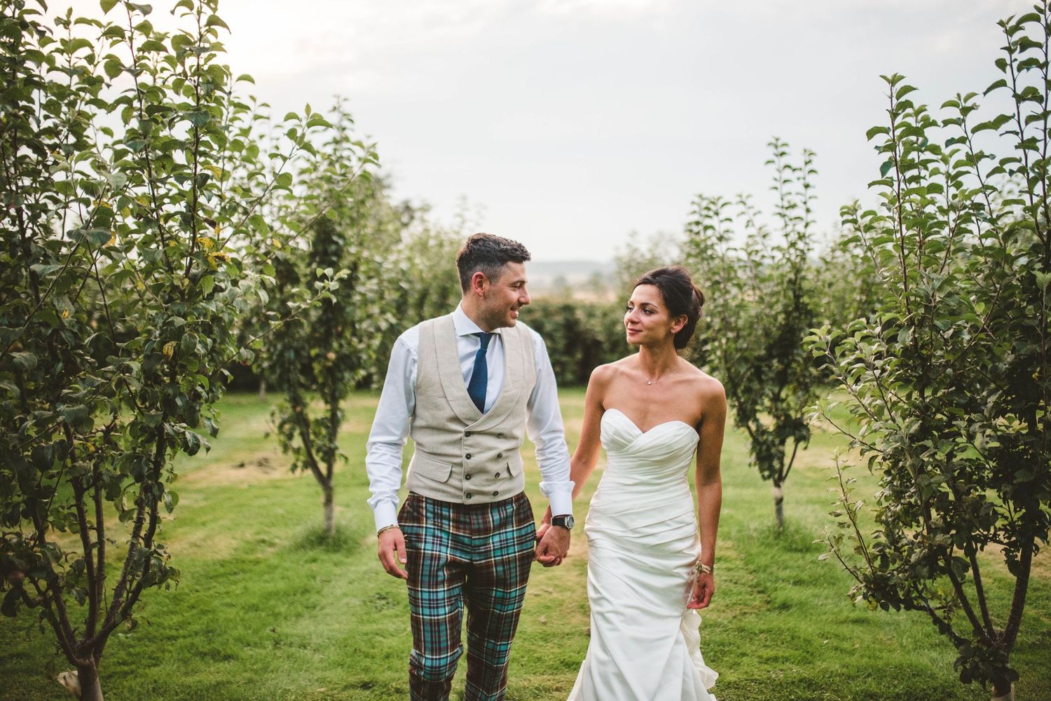 Couple walking through orchard in Scottish wedding attire.
