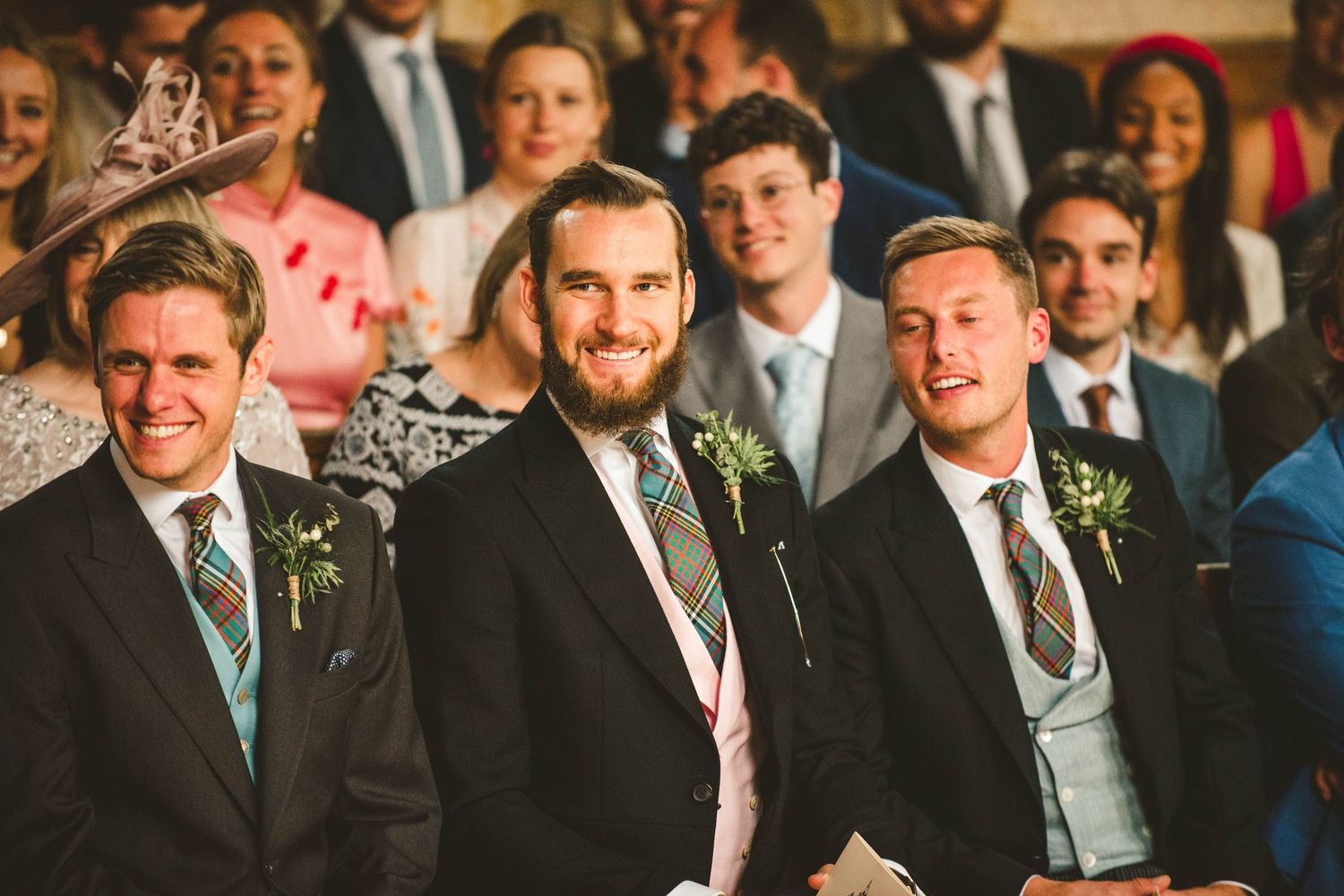 Wedding guests in formal attire and Scottish kilts seated in church pews.
