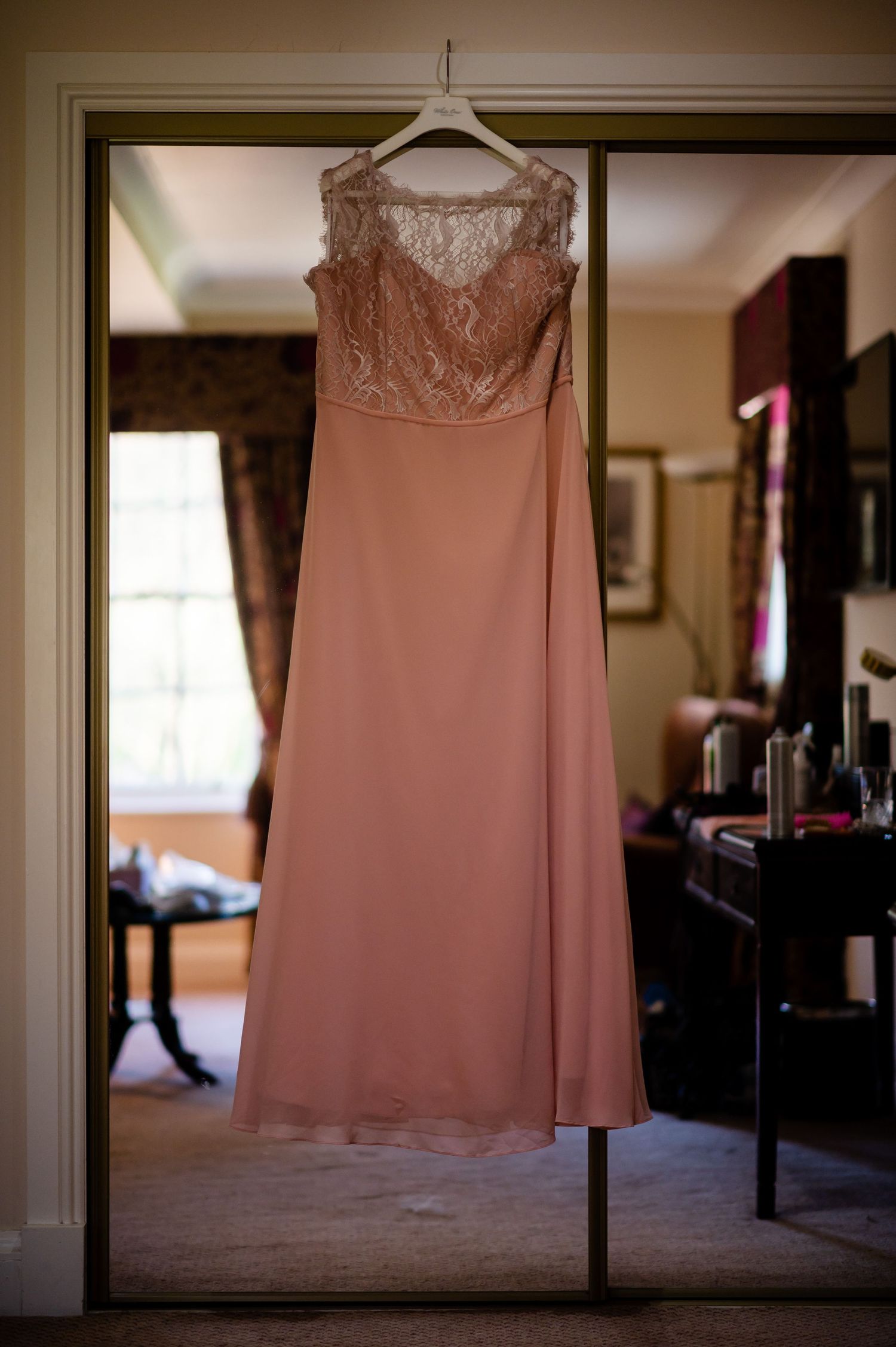 Blush pink formal dress with lace bodice hanging on display in doorway.