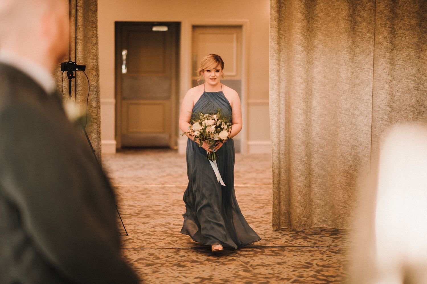 Elegant scene of someone in a navy gown walking down a hotel corridor.
