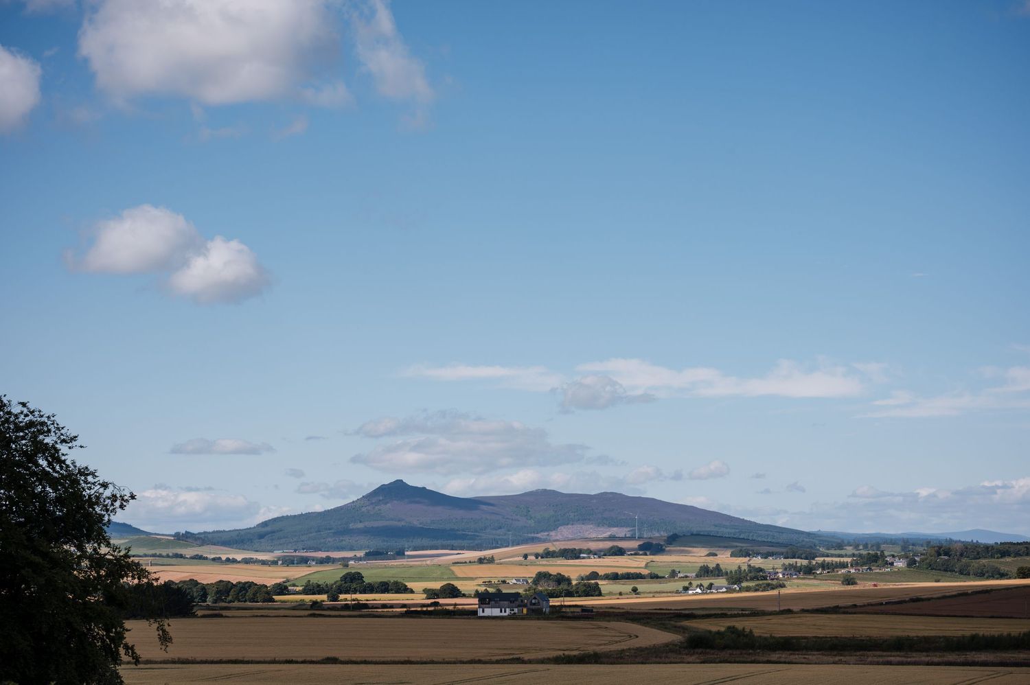 Rolling hills and mountains stretch across a rural landscape under a blue sky with scattered white clouds.
