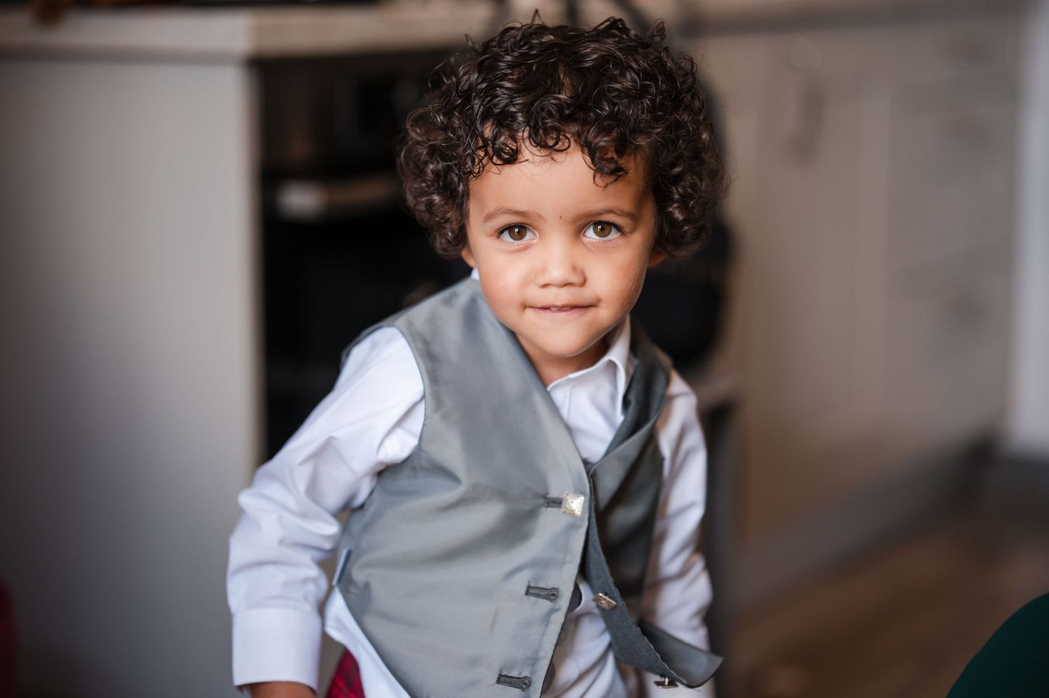 A young child wearing a gray vest and white shirt smiles at the camera.