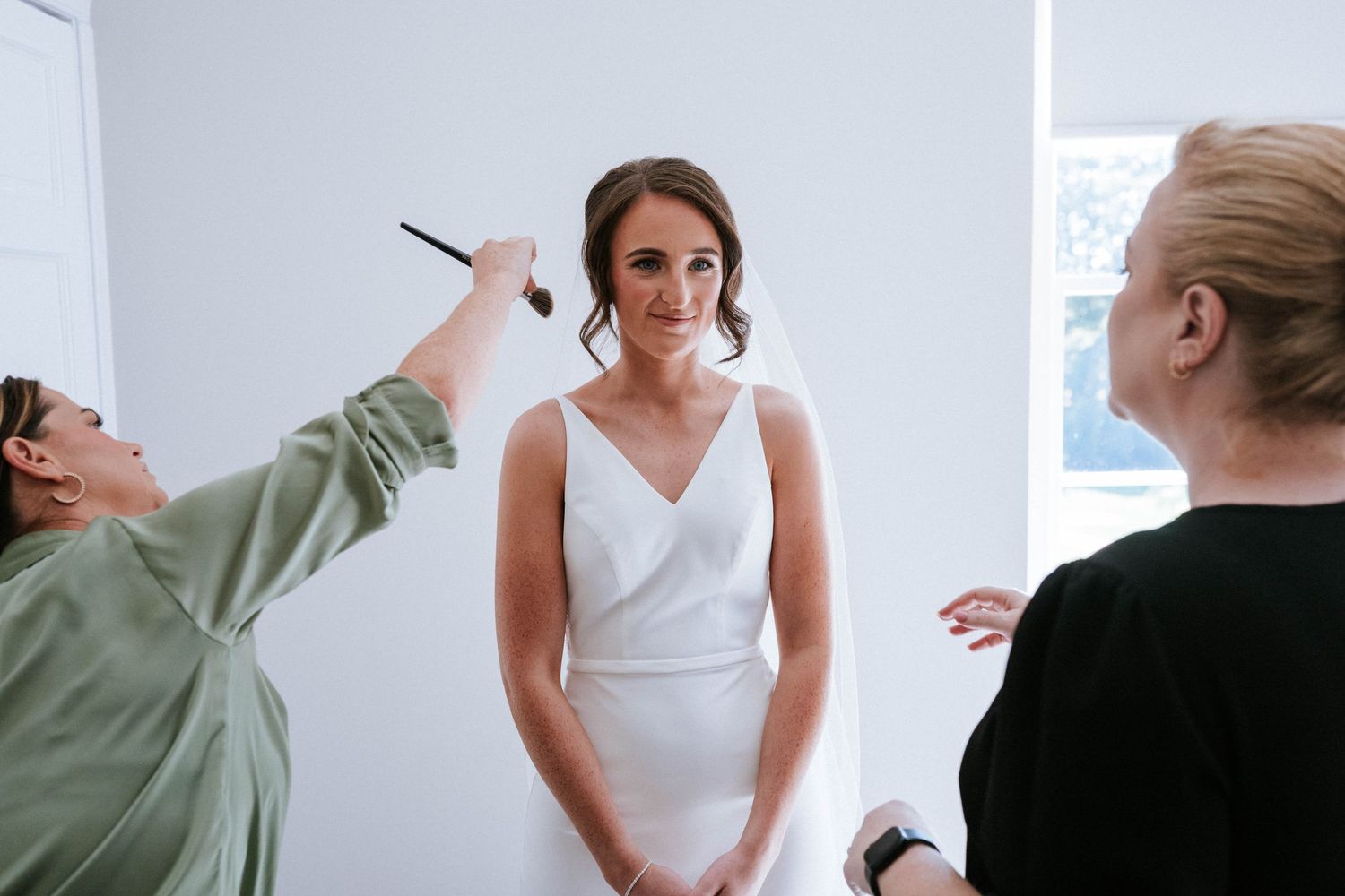 Wedding preparations showing final dress adjustments in a bright room.