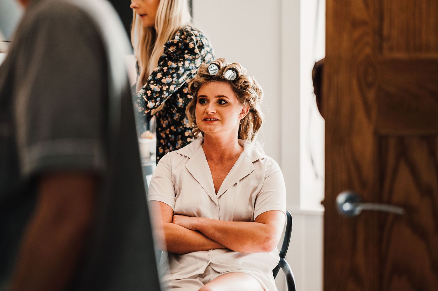 A person getting ready for a wedding sits in a chair while having their hair styled with rollers.