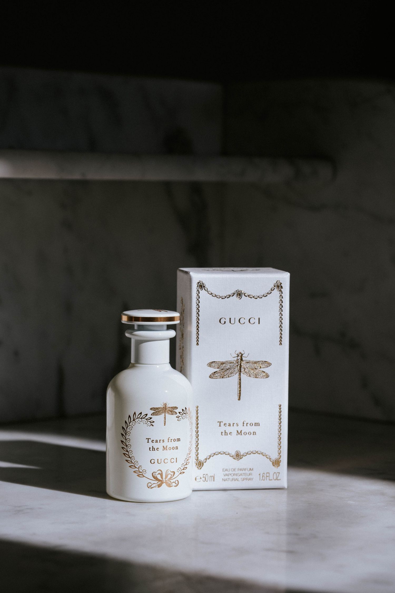 Gucci perfume bottles and boxes with gold dragonfly designs on white marble.