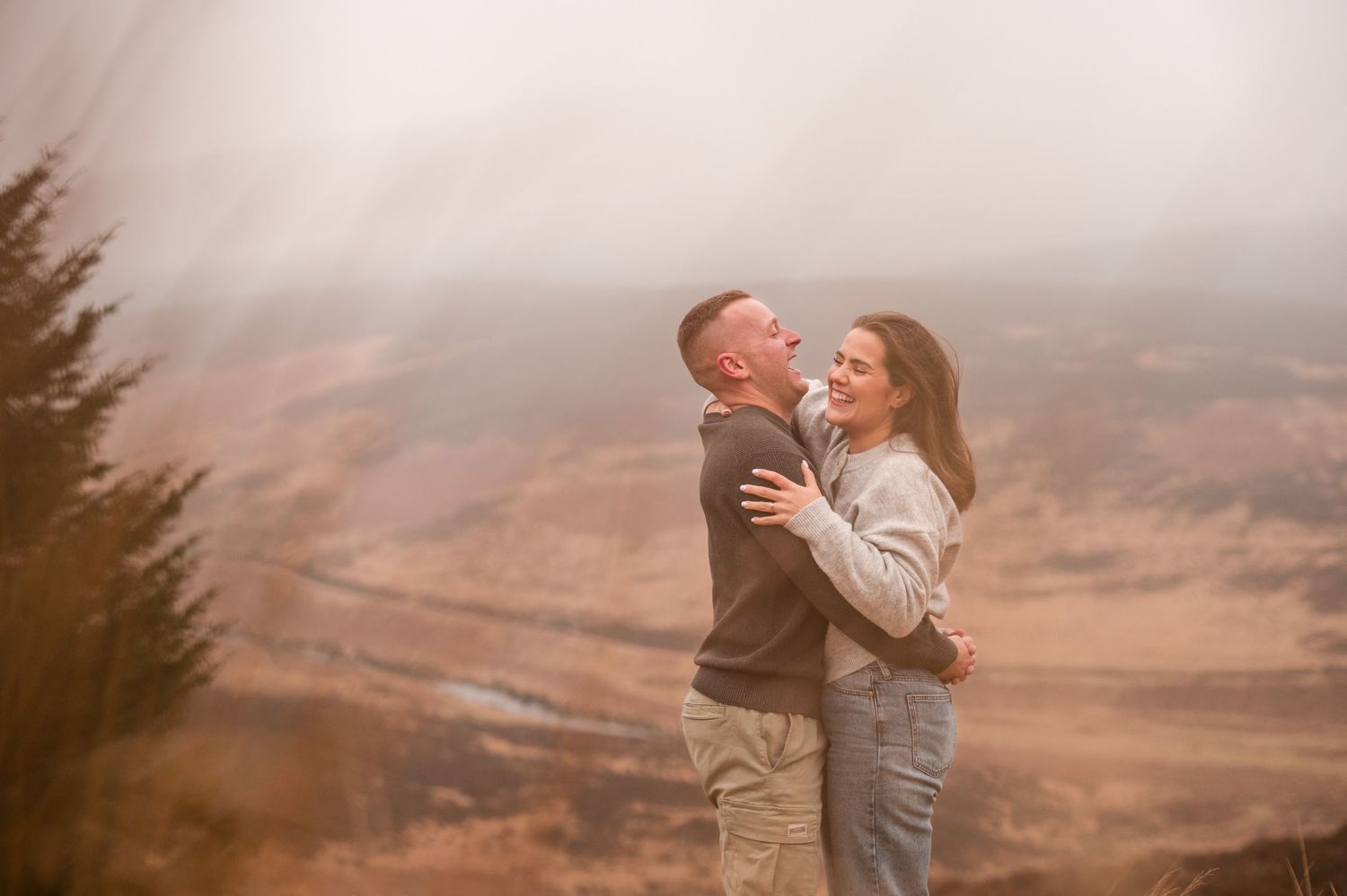 Engagement photography session Aberdeen. A couple shares an intimate moment overlooking a misty valley landscape.
