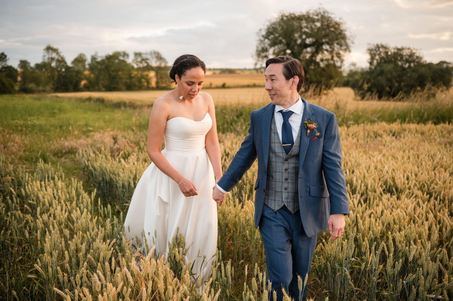 Couple walks through golden wheat field during sunset wedding photo session.