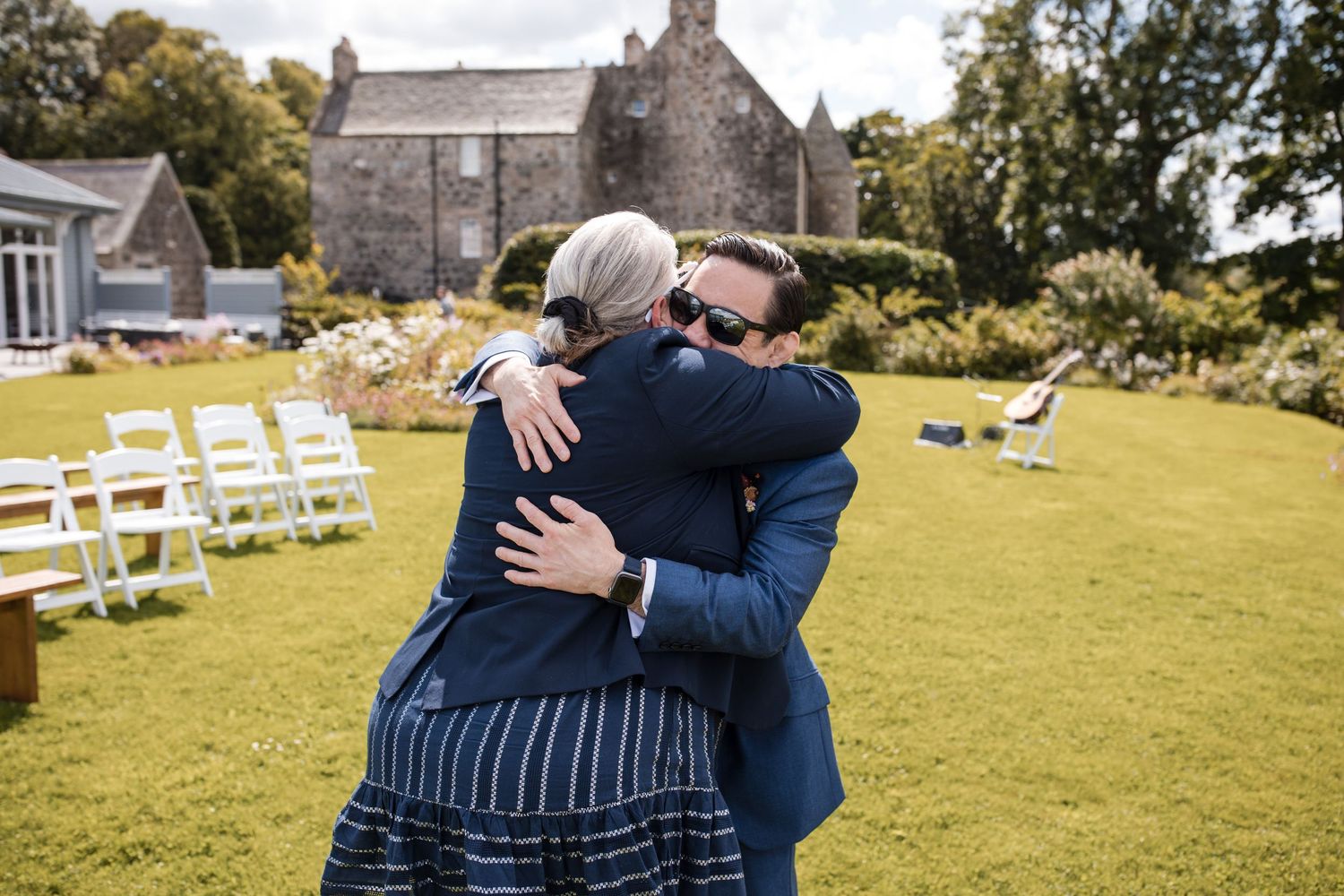 Emotional embraces and candid moments captured during an outdoor wedding ceremony on a grassy lawn.