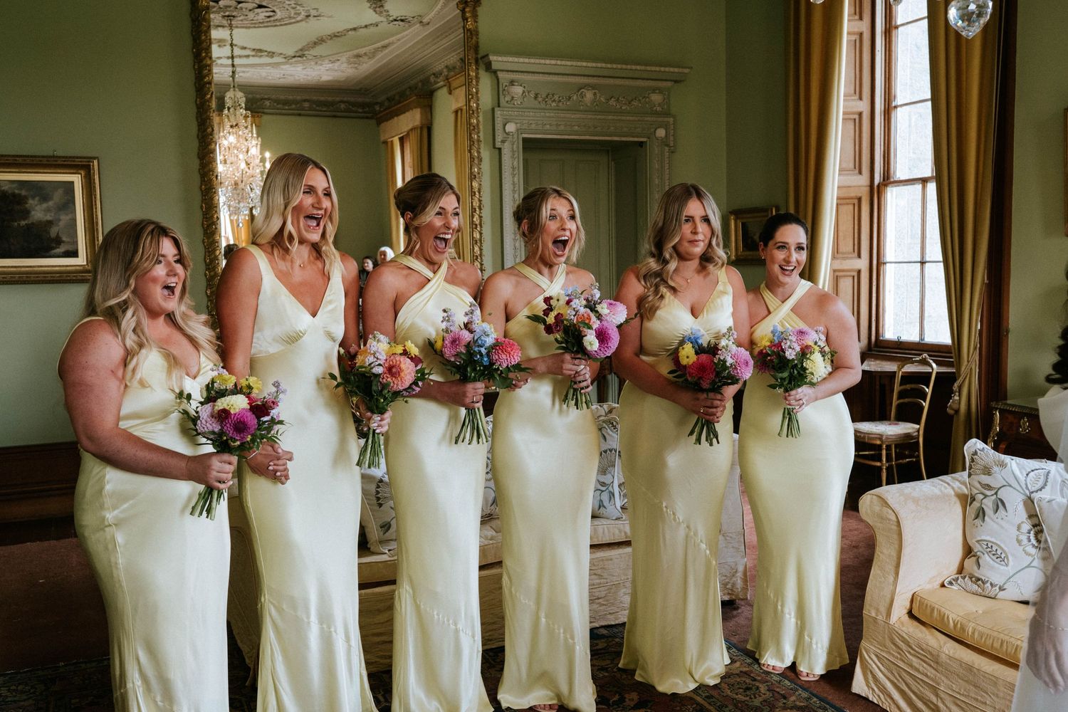 Bridesmaids in cream-colored dresses pose together holding colorful bouquets.