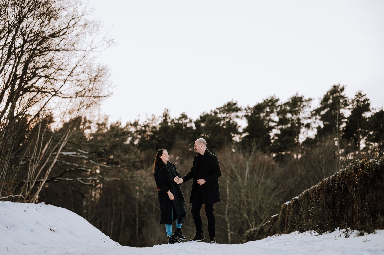 People walking along a snowy forest path during winter with bare trees and evergreens in the background.