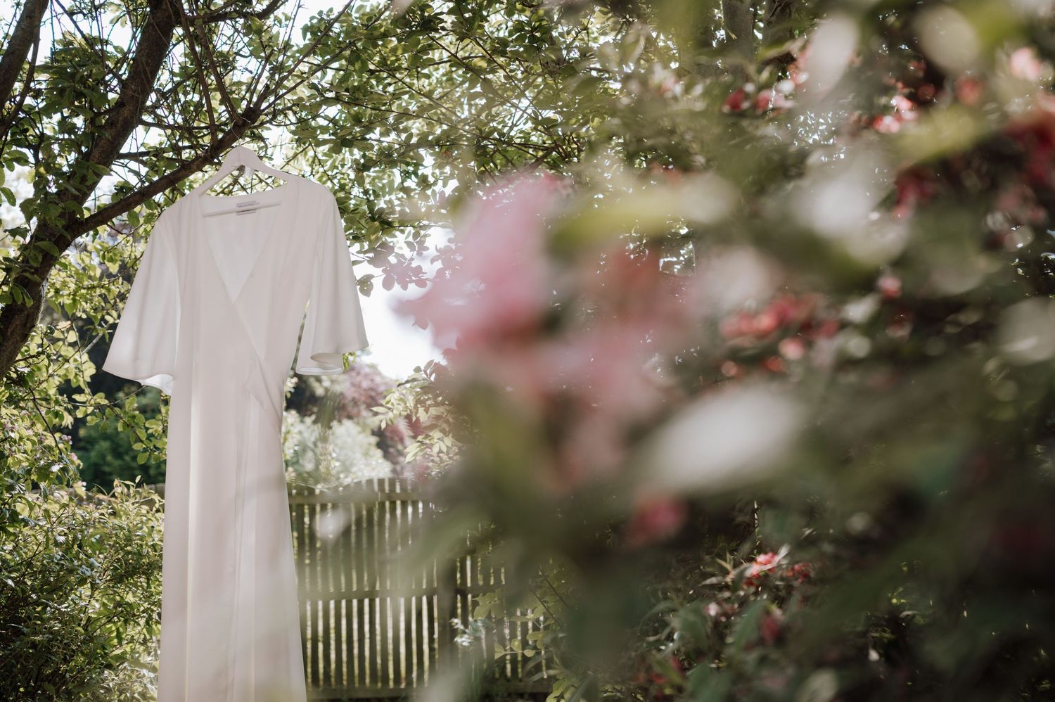 A serene garden scene with a white dress hanging among blooming trees and flowers.