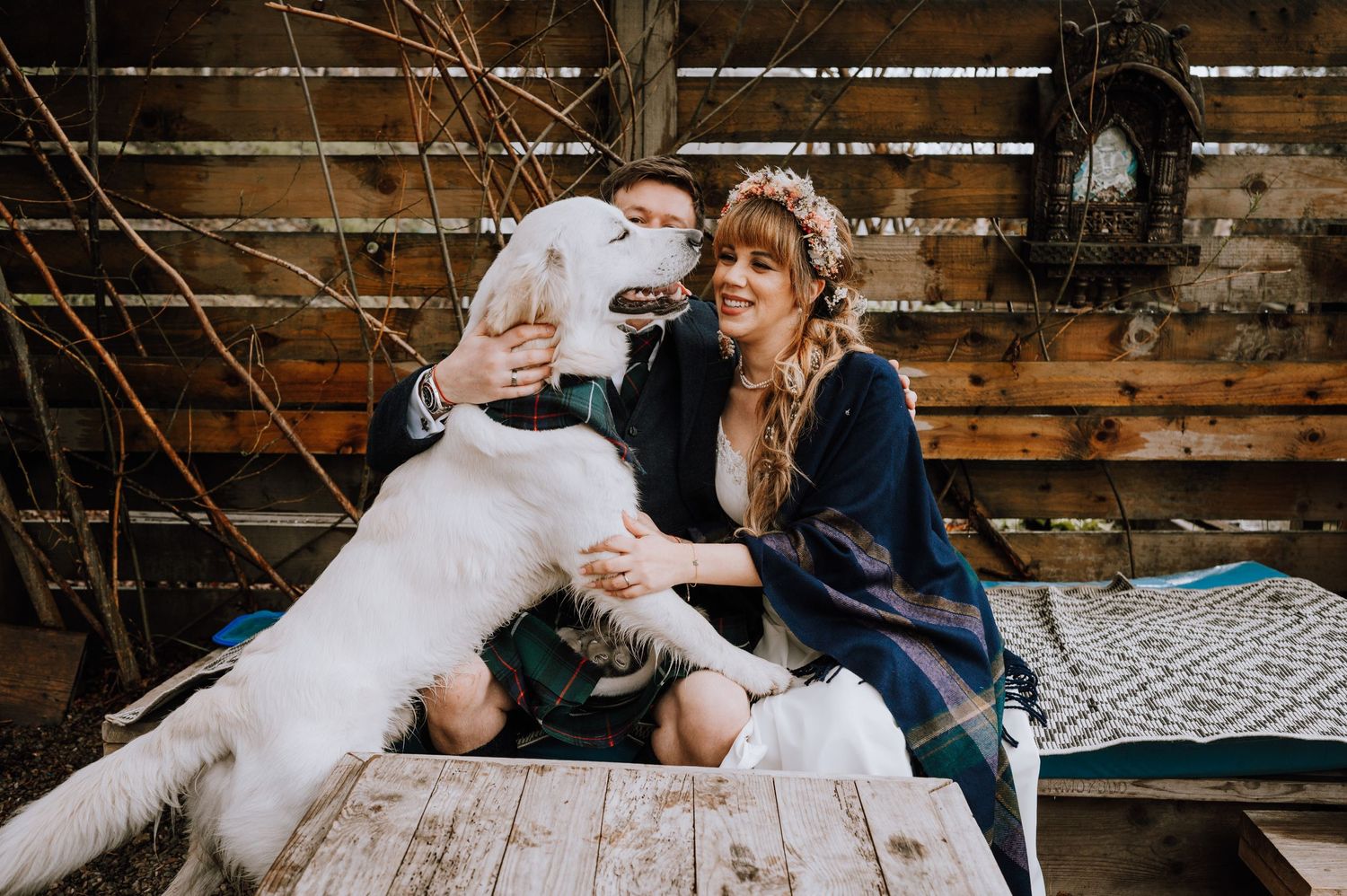Large white dog plays with couple on wooden deck during wedding photoshoot.
