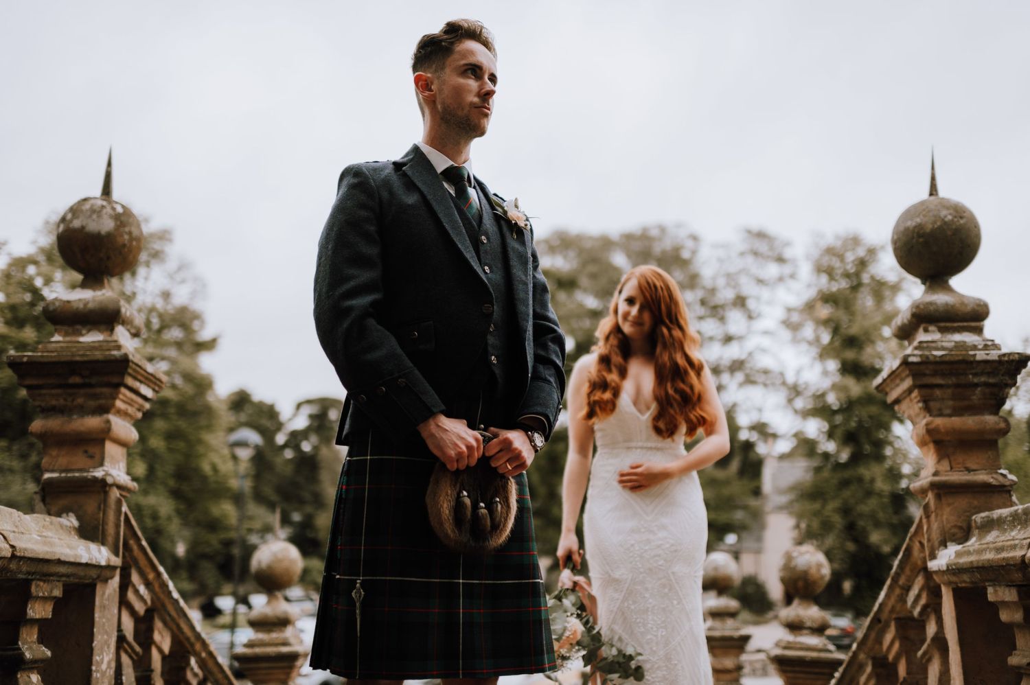 Scottish wedding couple on stone bridge with groom in traditional kilt.