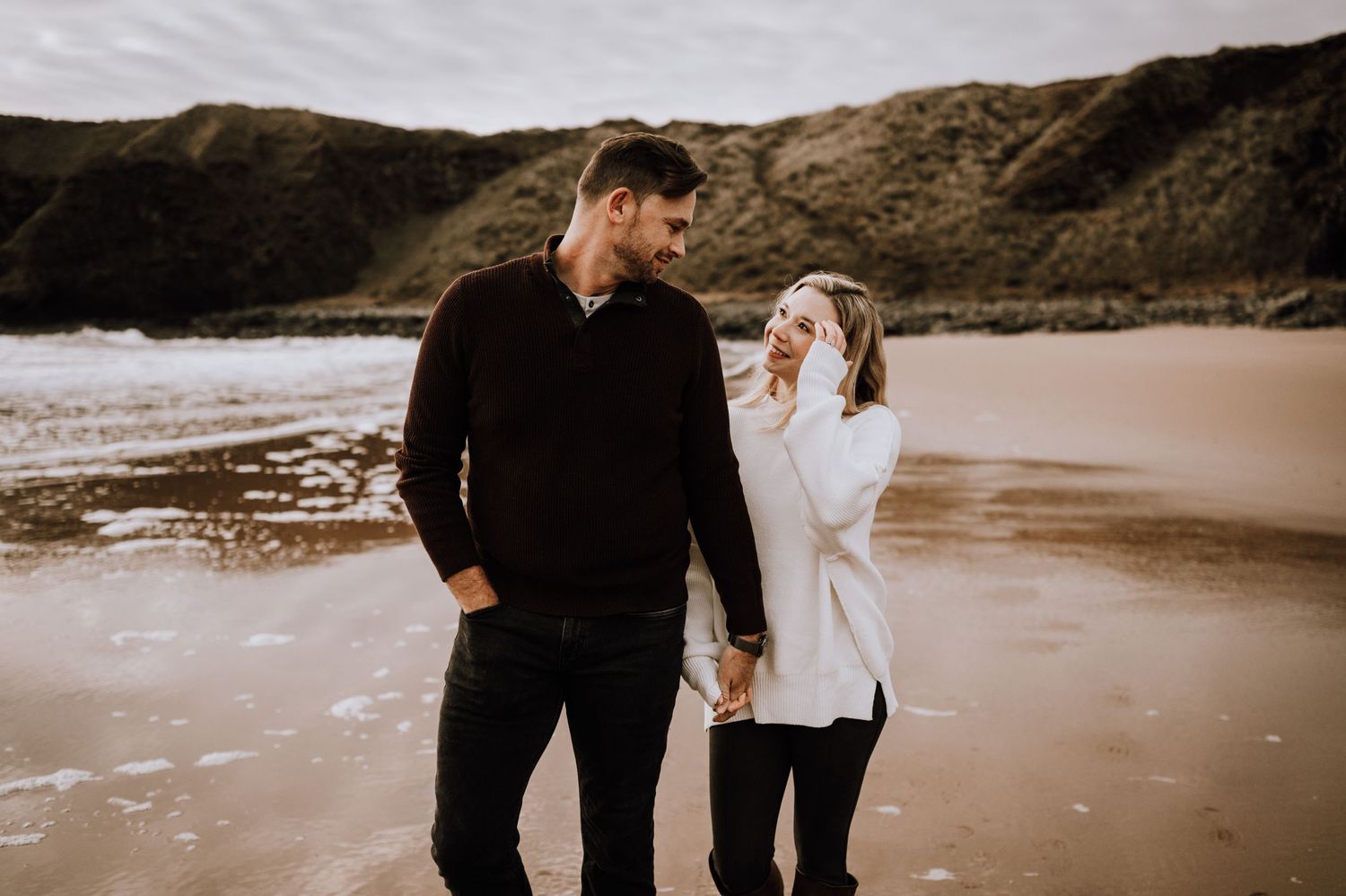 Couple sharing a laugh while walking hand in hand on a scenic beach.