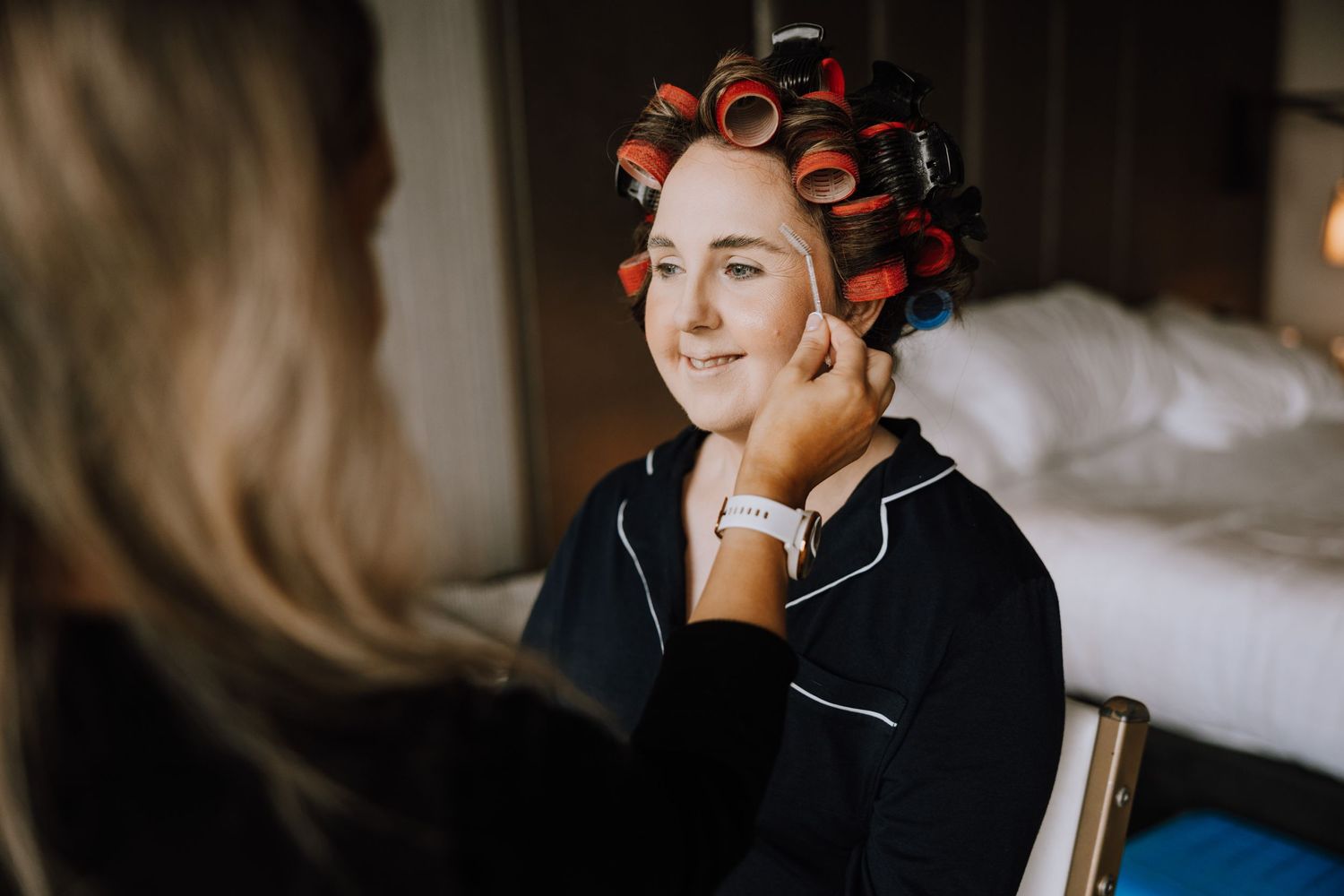 Someone wearing hair rollers gets their makeup done while wearing black silk pajamas.