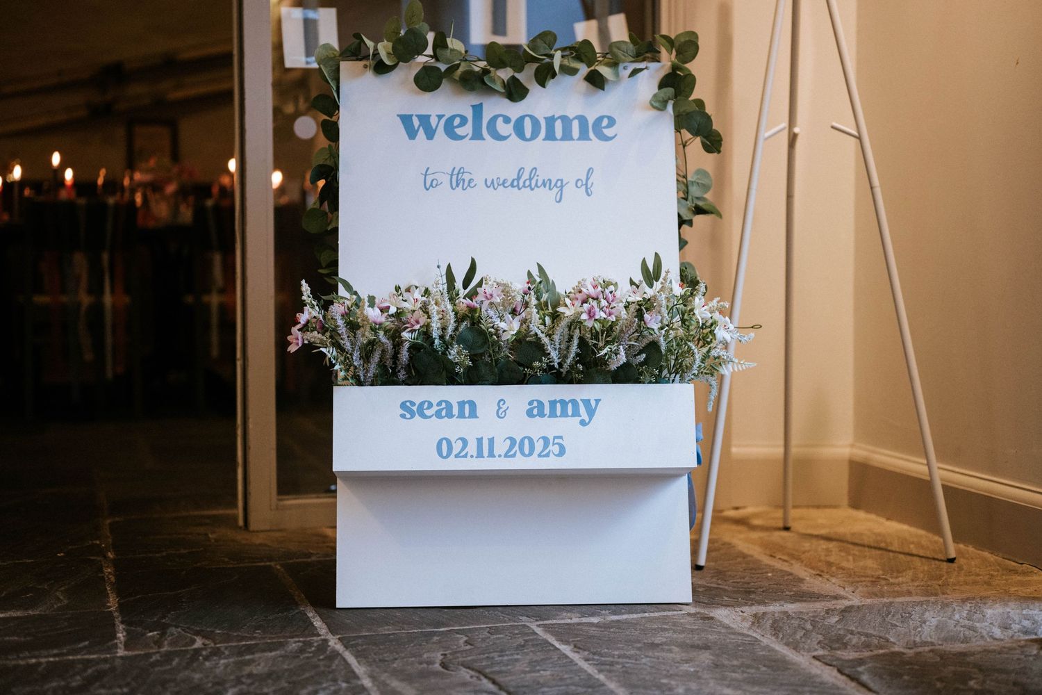 Welcome sign and floral decorations at wedding venue entrance.