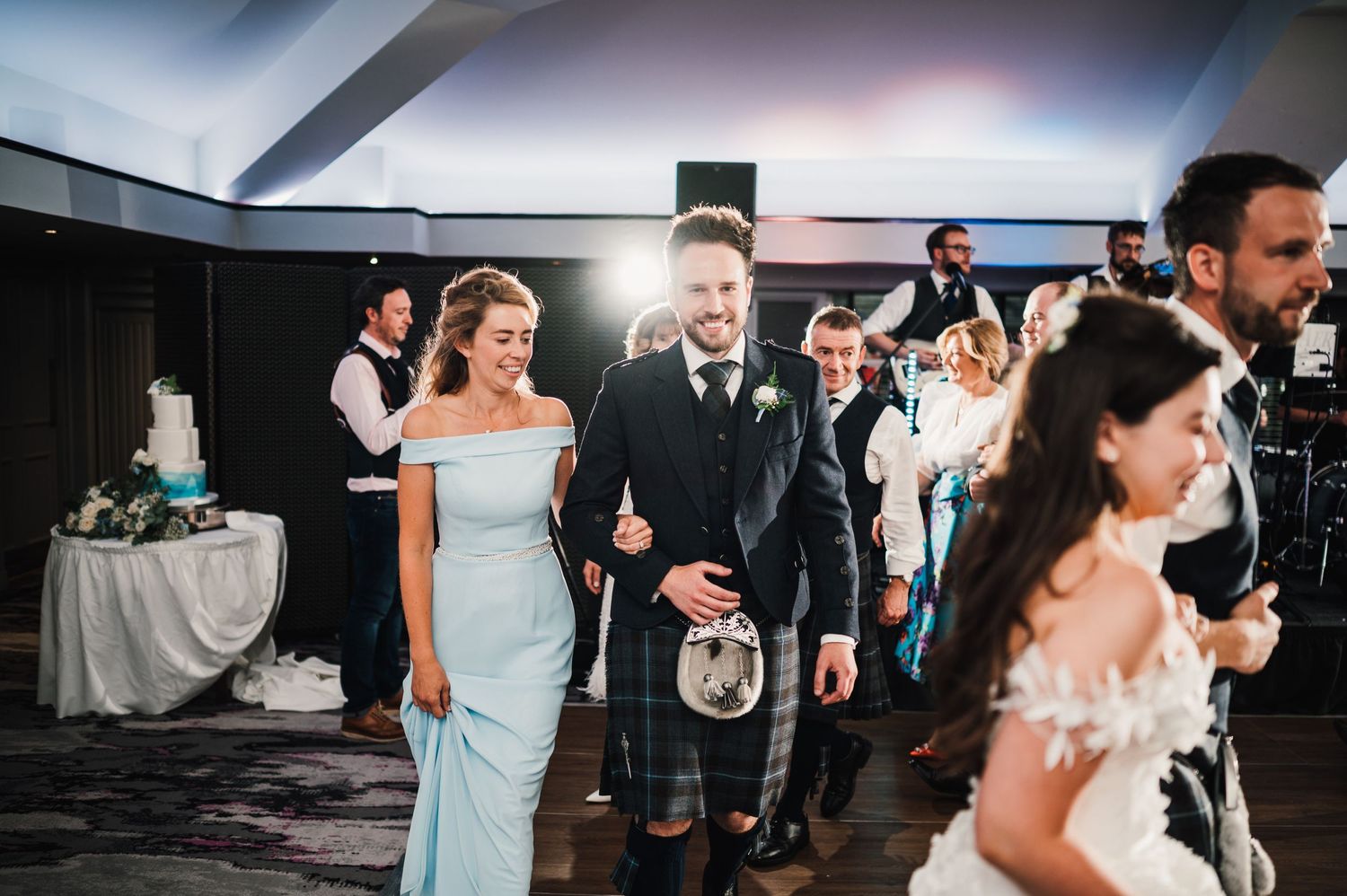 Wedding party members walk across dance floor during reception celebration.