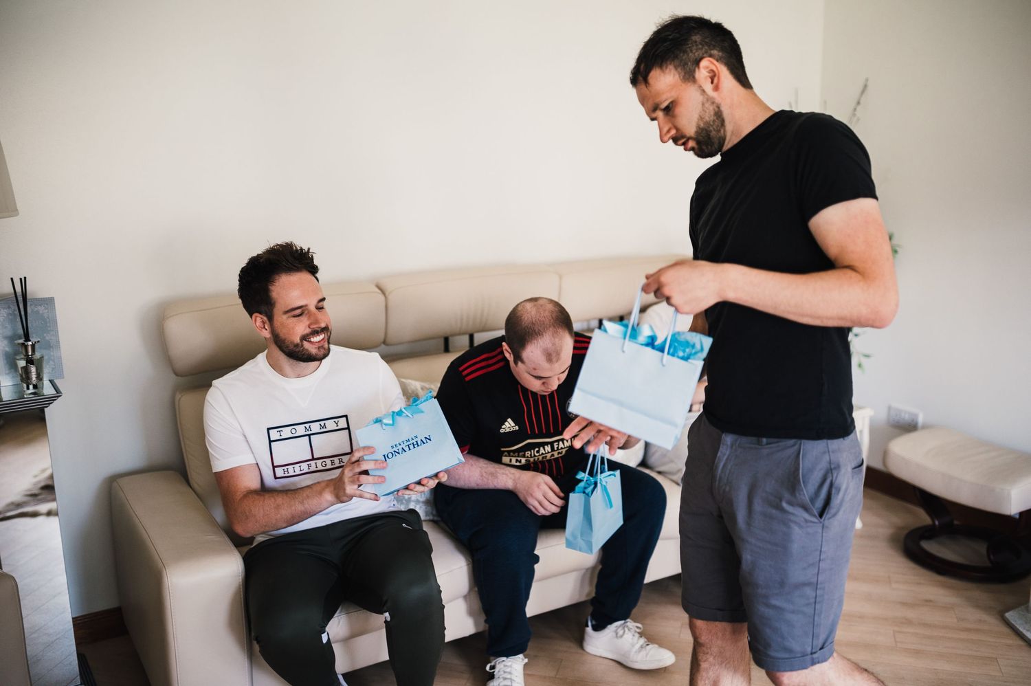 Three people sitting on couch examining bright blue gift bags together.