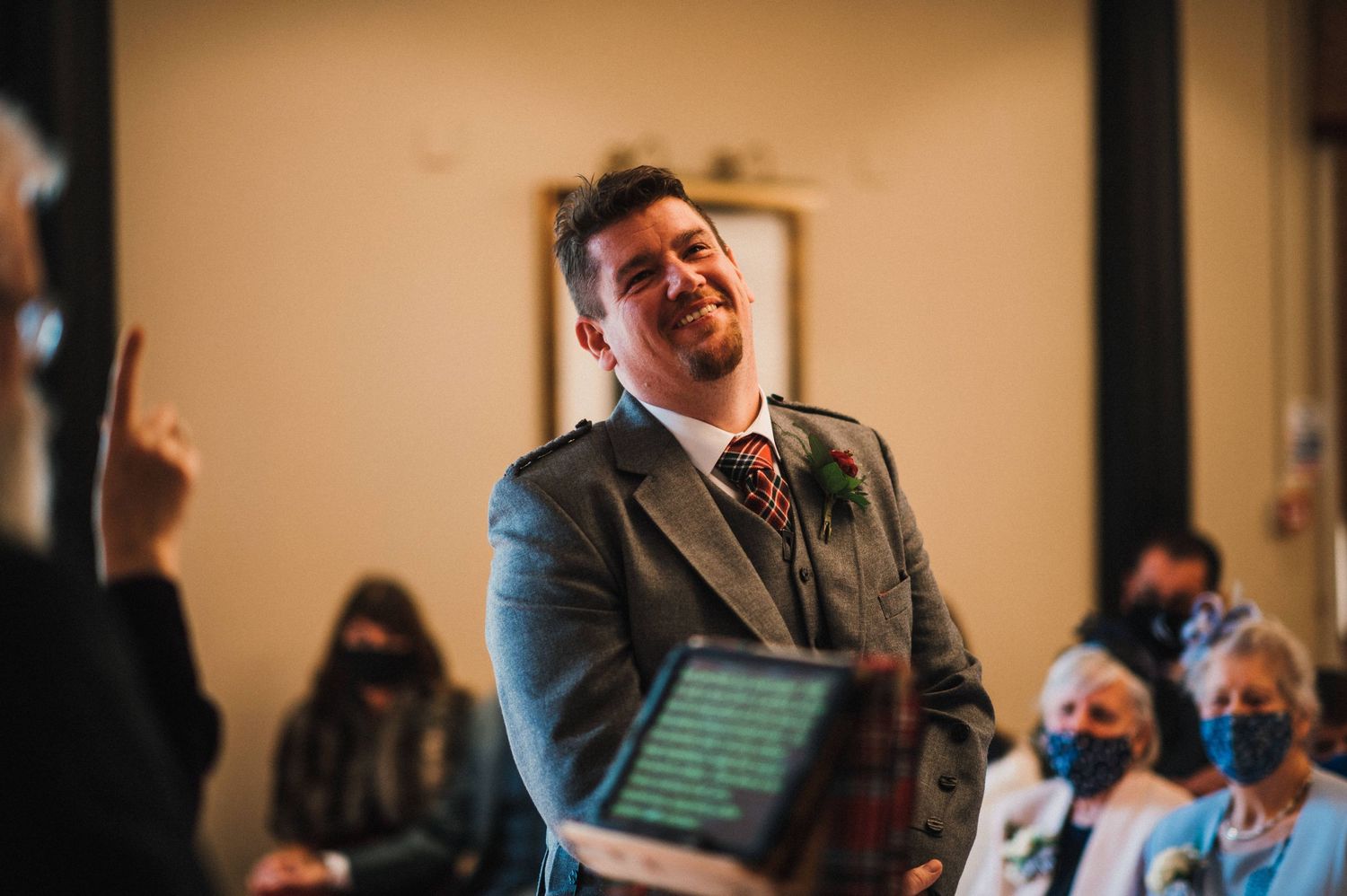 A heartfelt moment during a wedding ceremony with masked guests in the background.