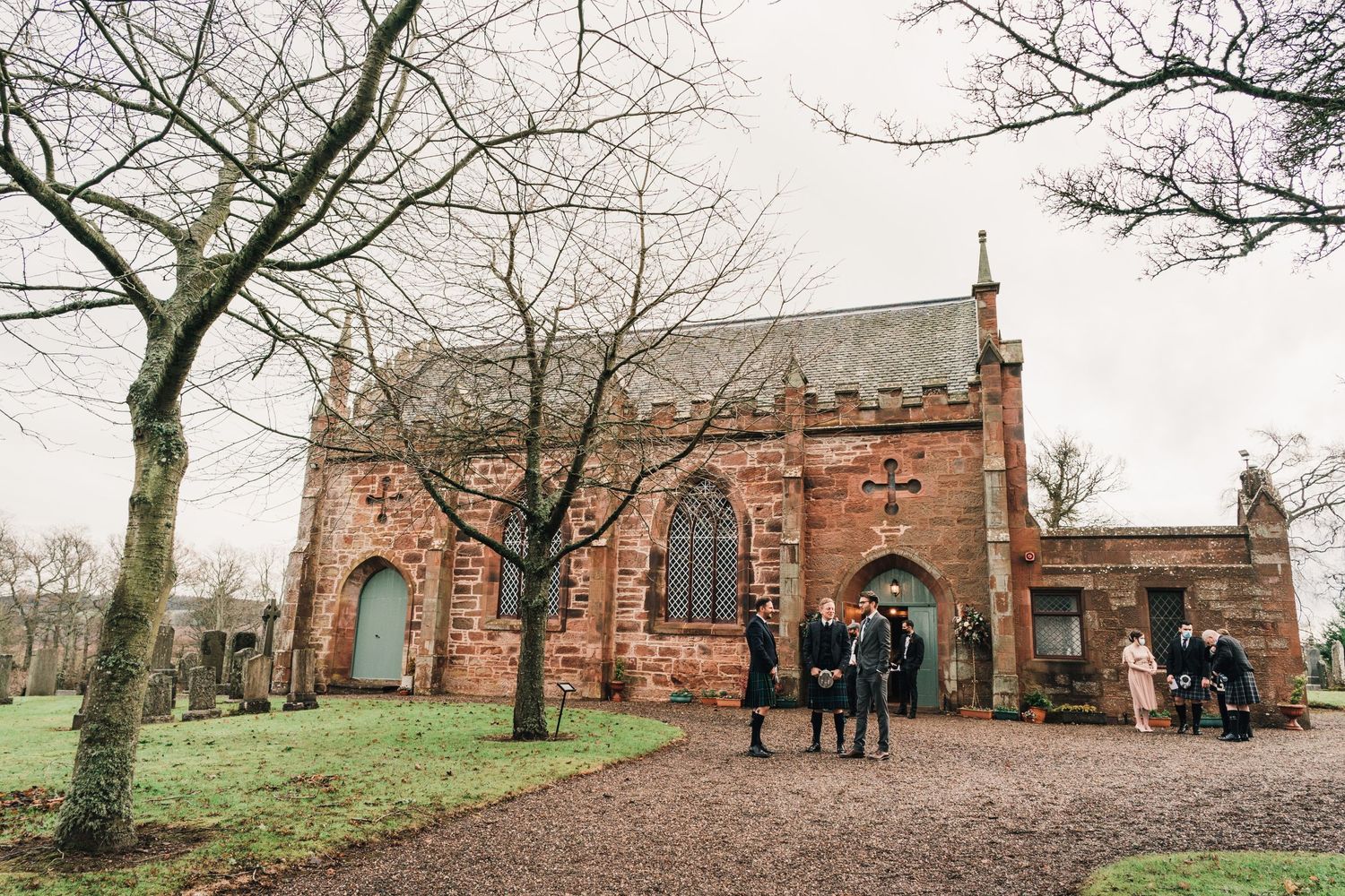 Gothic red sandstone church exterior with guests gathering on path during winter.
