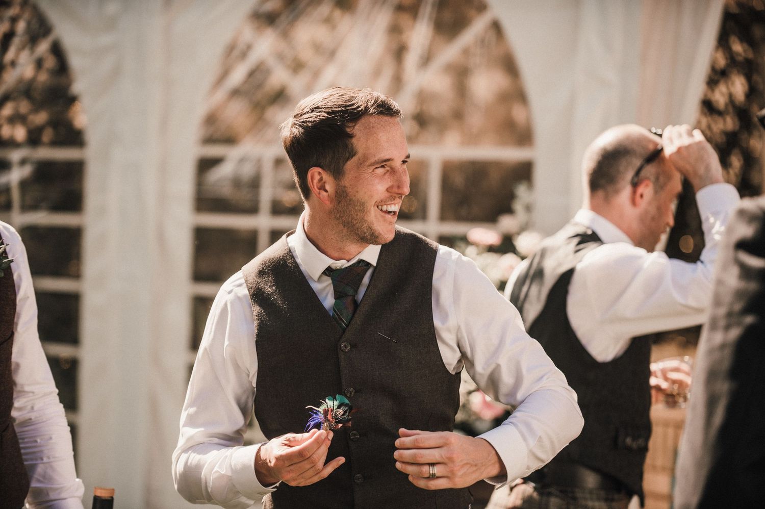 Wedding guest in formal attire smiling while holding drinks at an elegant reception.