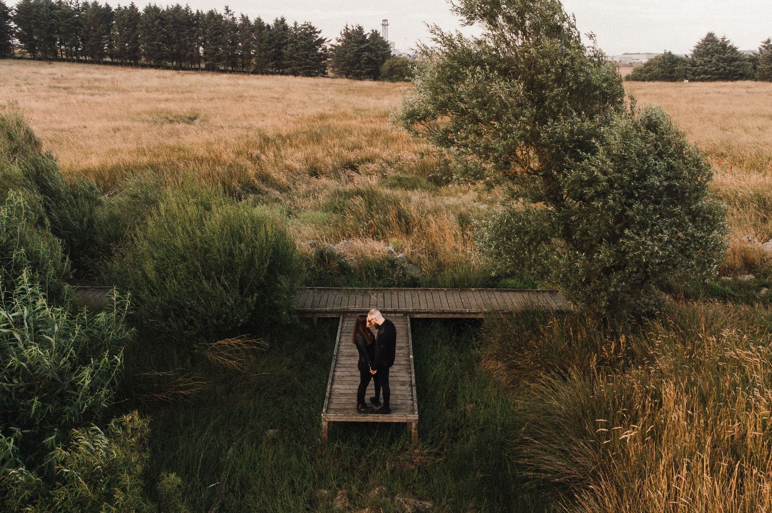 Aerial view of couple standing on wooden platform in golden meadow.