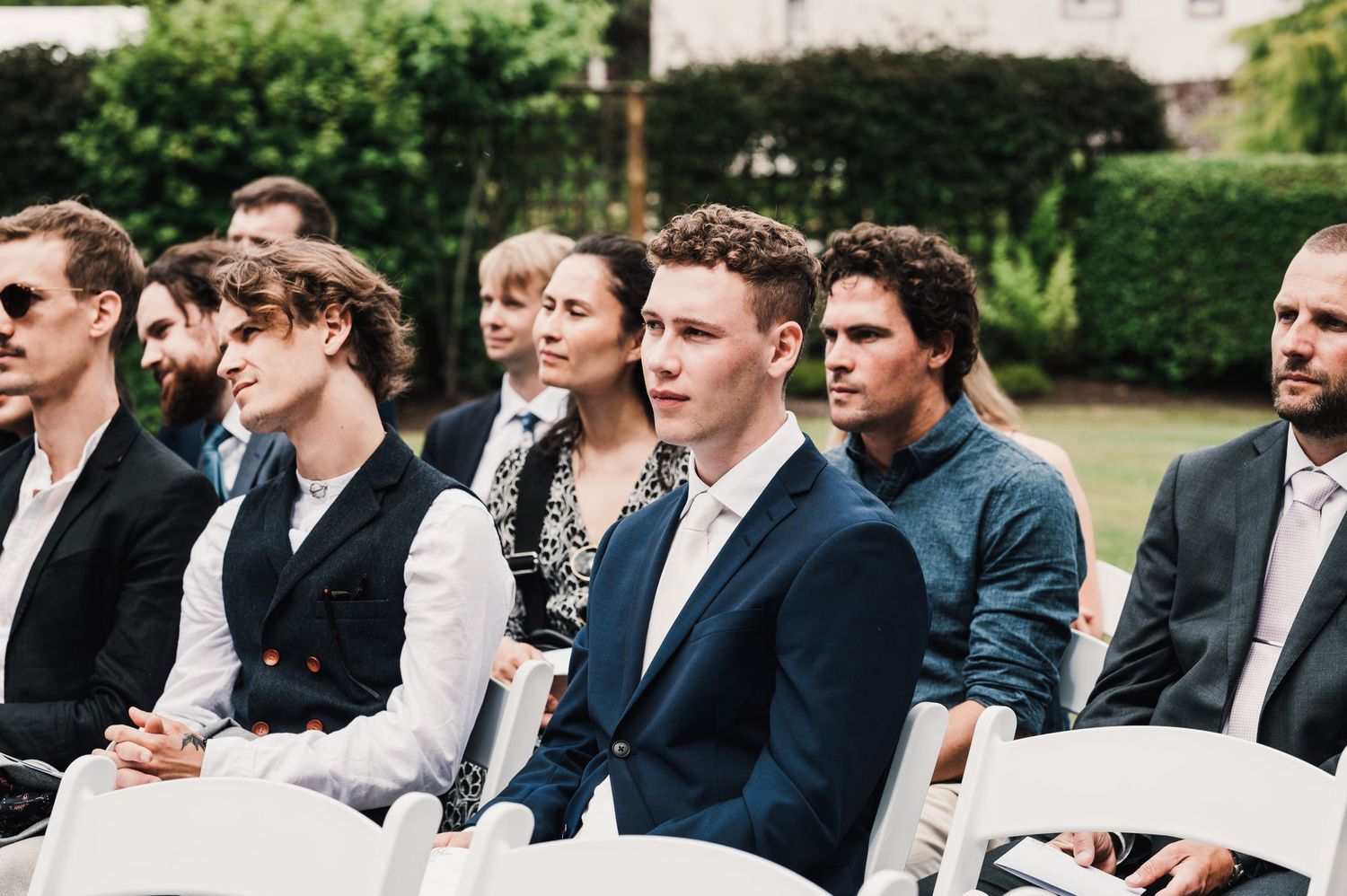 Wedding guests seated in rows of white chairs watching outdoor ceremony.