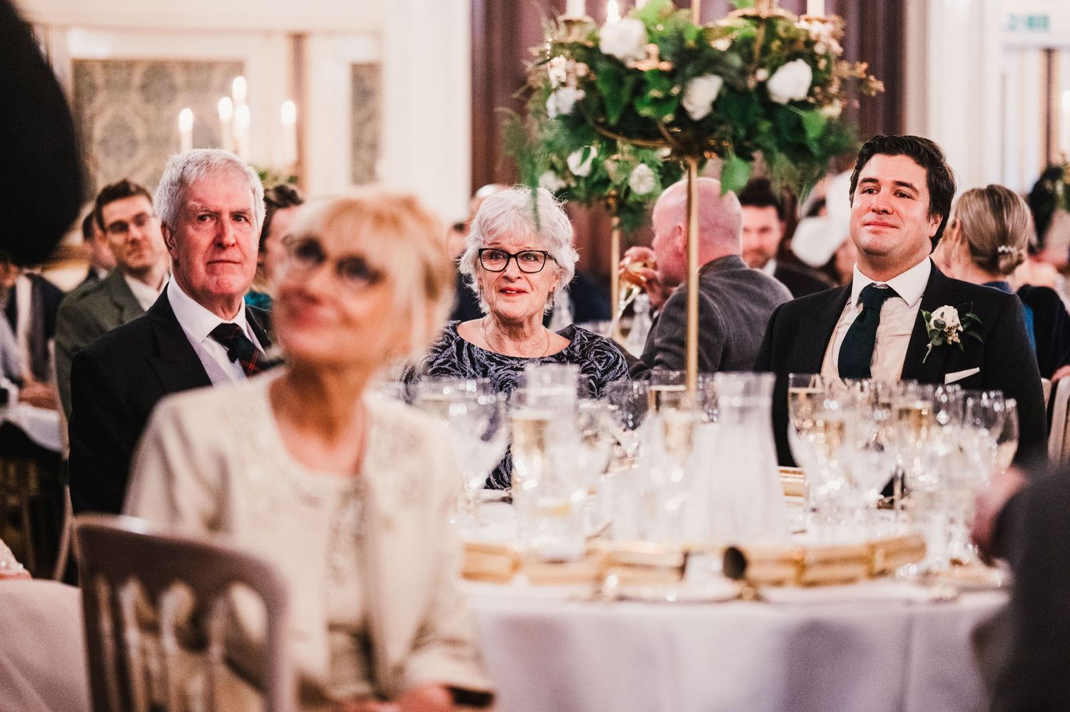 Guests seated at round tables during formal dinner with floral centerpieces and candlelight.