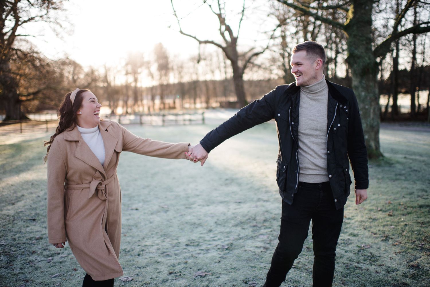 A playful moment between a couple on a winter path with sunlight streaming through trees.