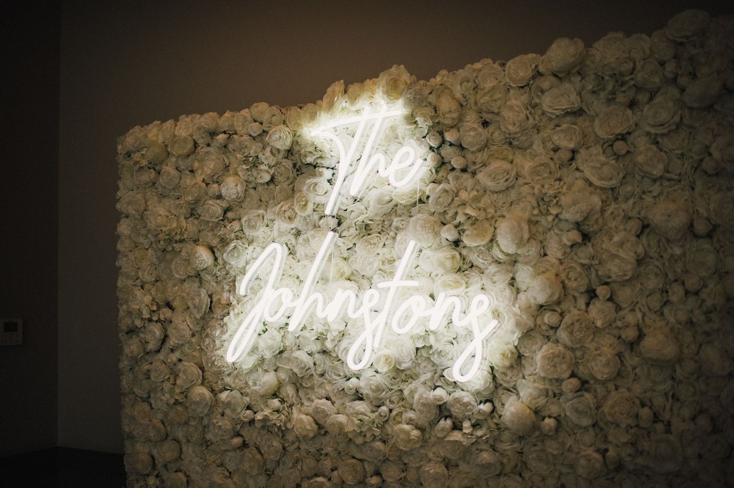 Glowing neon 'The Chapter' sign mounted on a white floral wall backdrop creates an elegant wedding atmosphere.