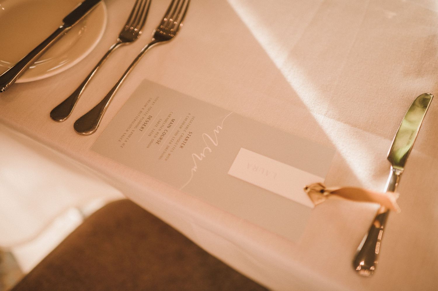 Elegant place setting with silverware and menu on a light colored tablecloth.