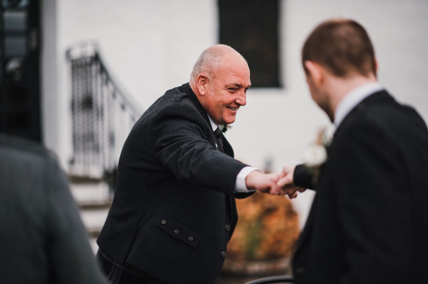 A person in formal black attire gestures animatedly outside a white building.