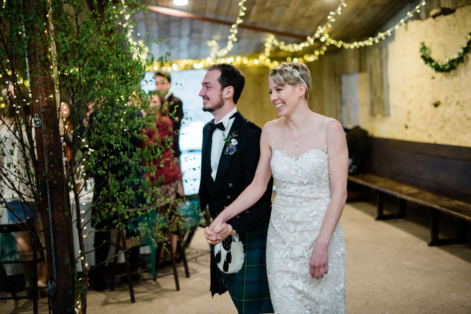 A wedding reception in a rustic venue decorated with greenery and twinkling lights.