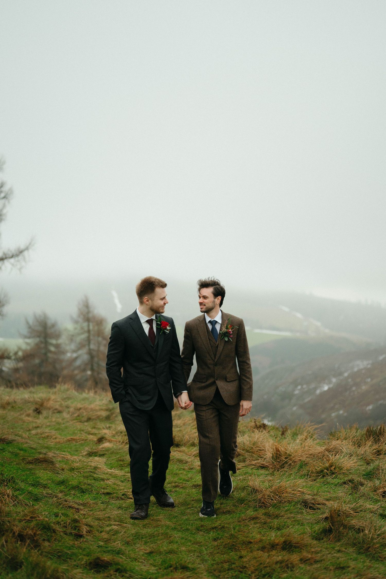 Drumtochty Castle  Wedding Photography. A couple walks together on a hilltop wearing formal suits with mountains in the background.