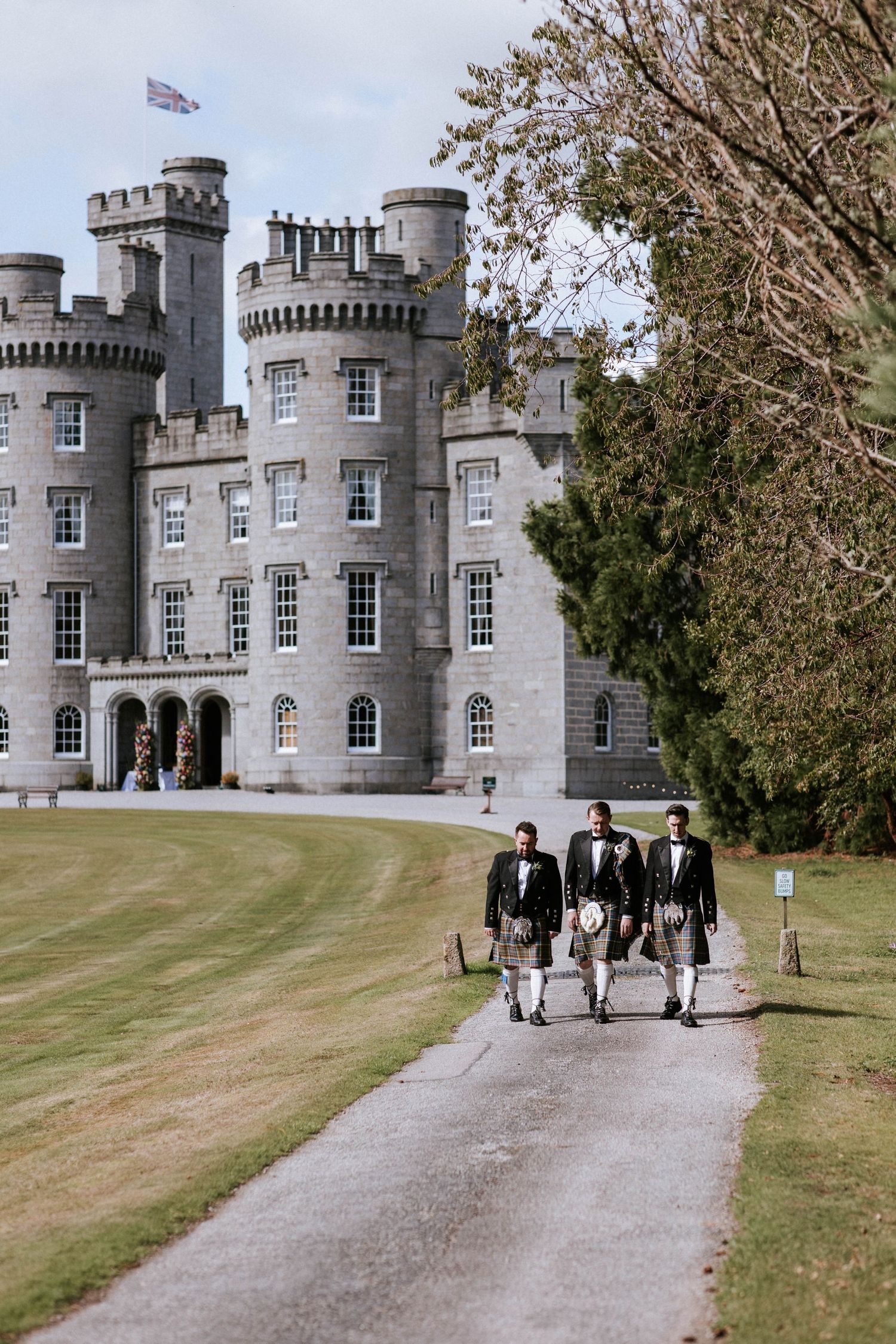 Wedding party approaching a majestic stone castle with turrets and arched windows.