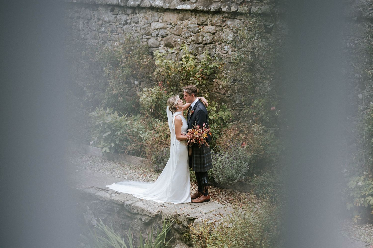 Couple photographed through foliage during outdoor wedding portraits.