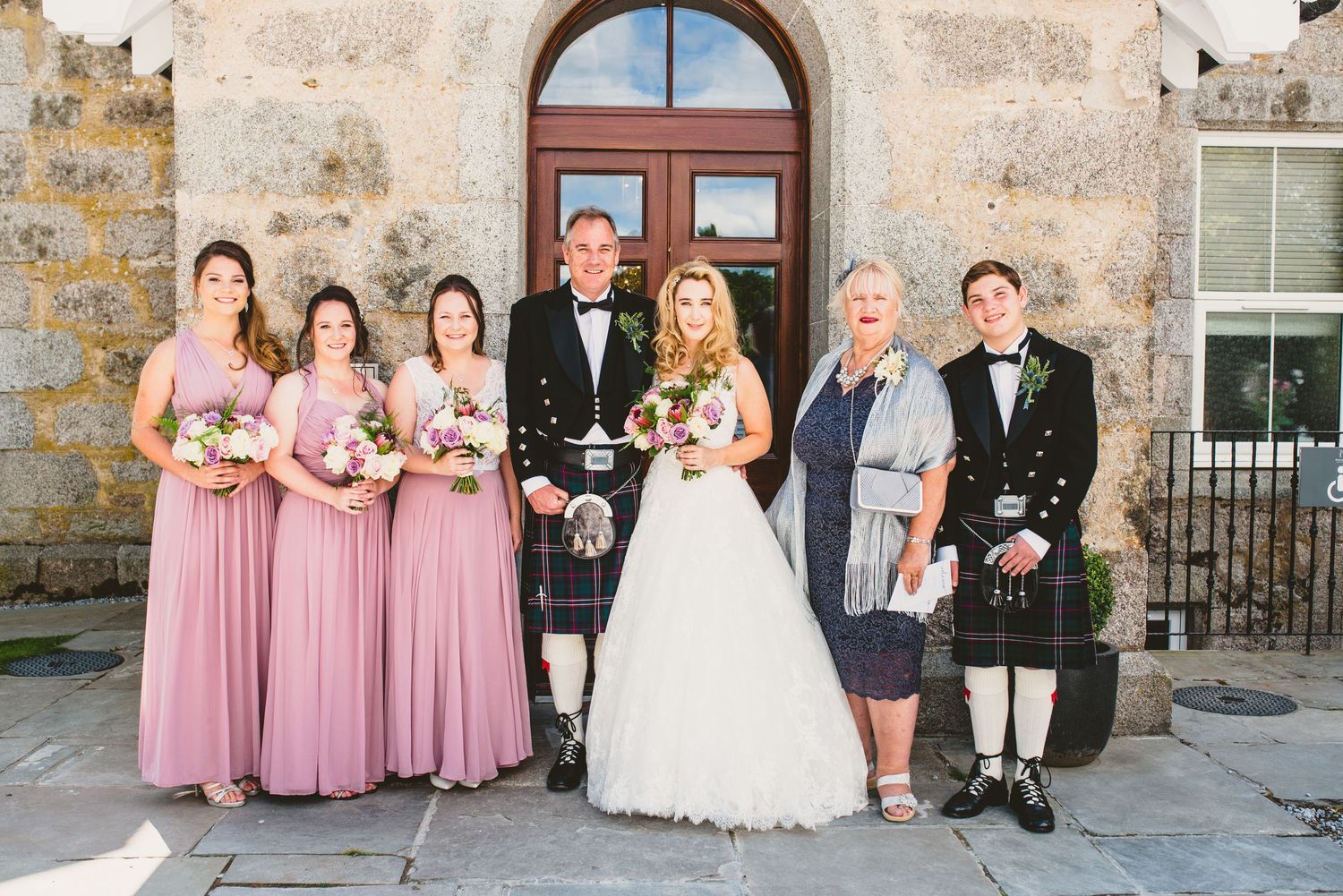 Wedding party poses in front of rustic stone building with pink bridesmaid dresses.