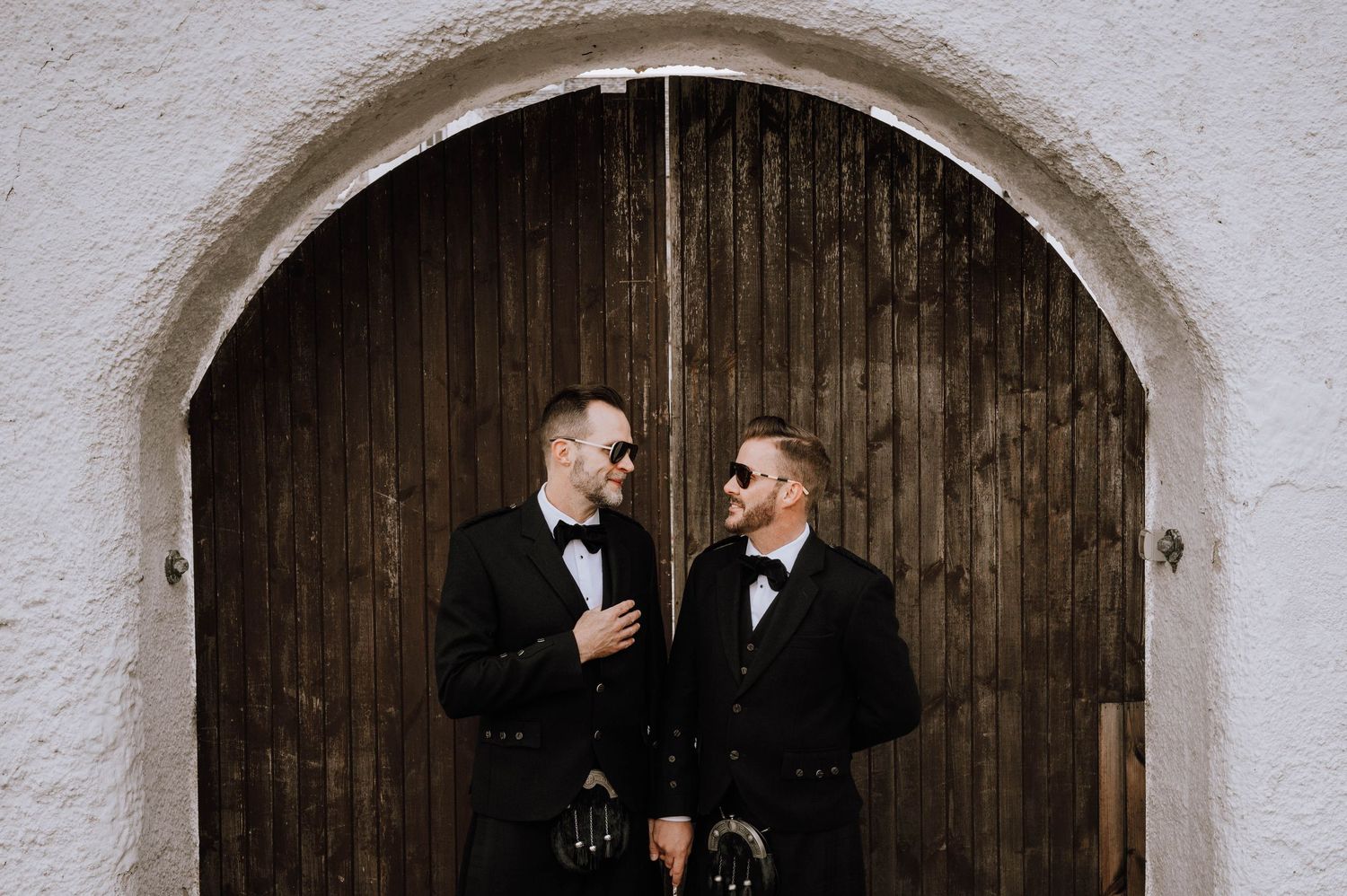 Logie House Wedding Photography. A couple in formal attire stands beneath stone archways at a historic venue.