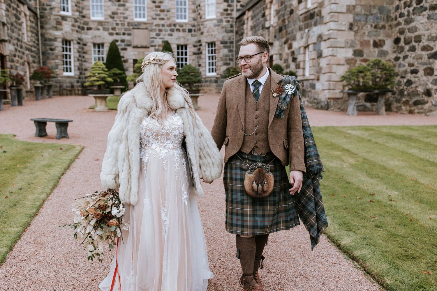 Couple celebrates their wedding day on a gravel path beside a historic stone building.