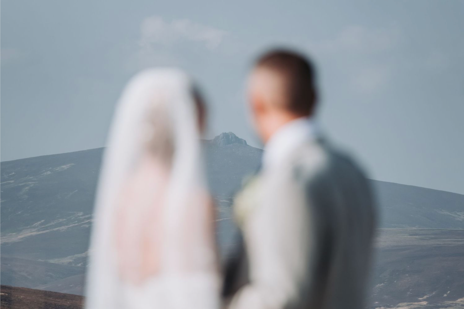 A blurred artistic wedding photo shows a couple in white against a mountainous background on their special day.