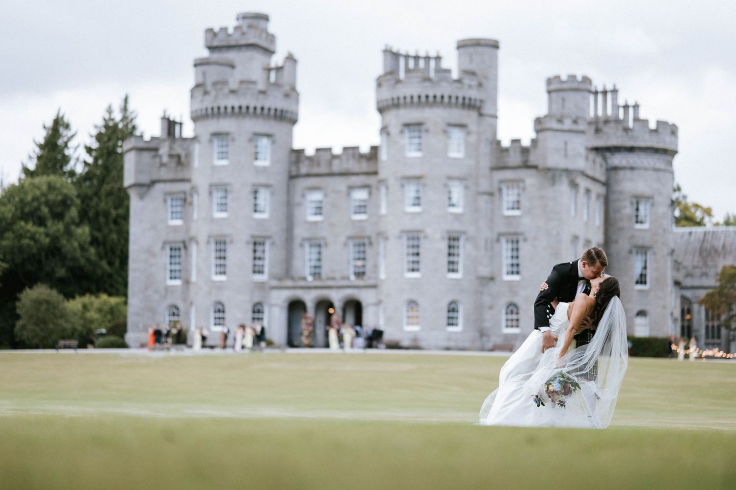 A grand Scottish castle with gray stone towers serves as an elegant wedding venue on a sunny day.