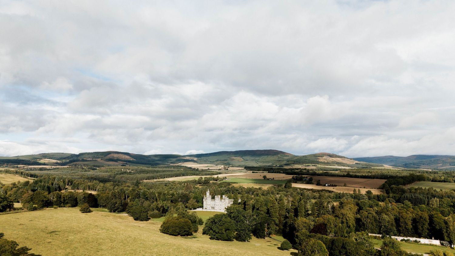 Sweeping landscape view of rolling hills and countryside surrounding a historic castle estate.