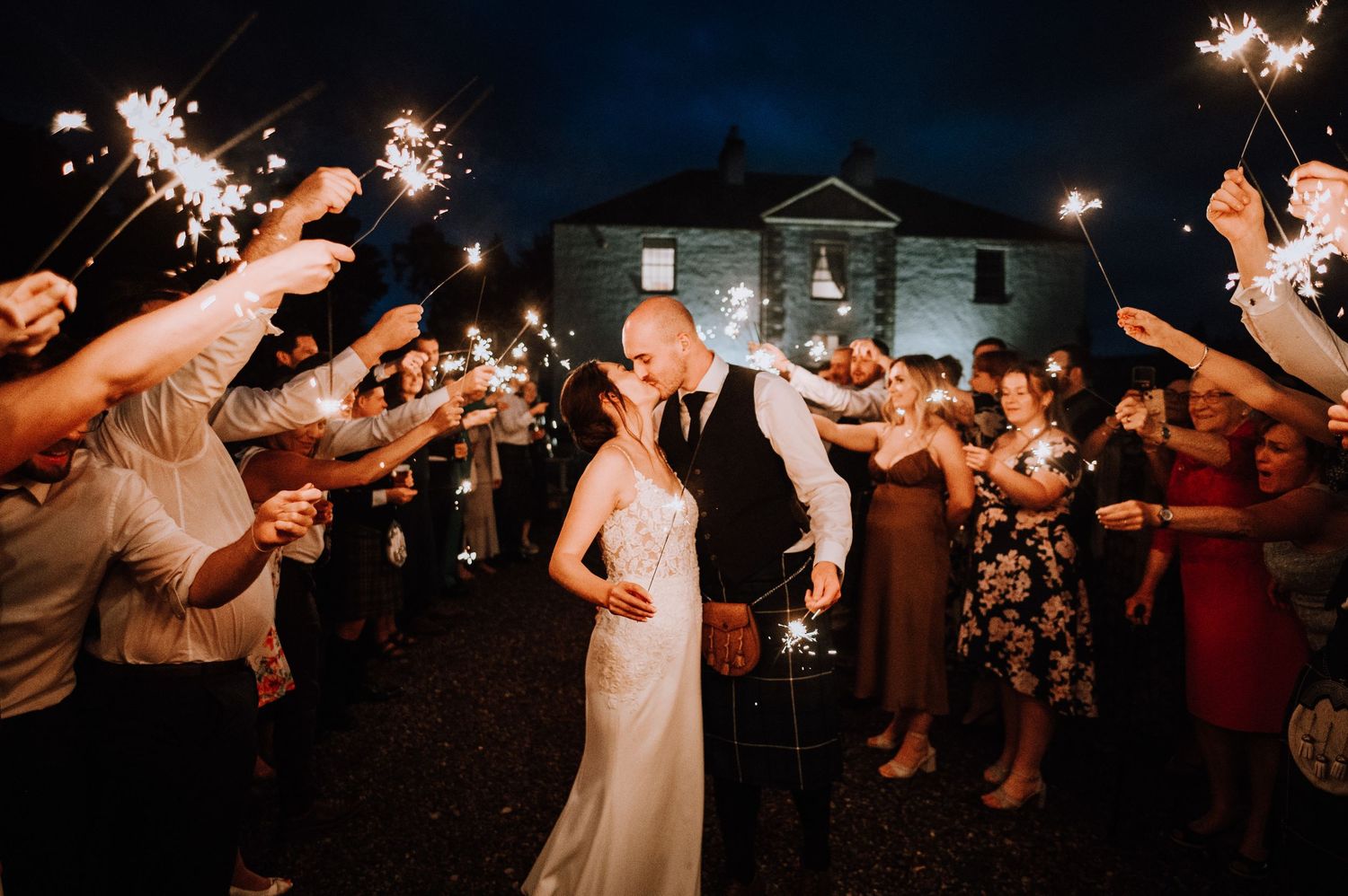 Aberdeen Wedding Photography. Guests hold sparklers creating a magical nighttime exit tunnel at an outdoor wedding celebration.
