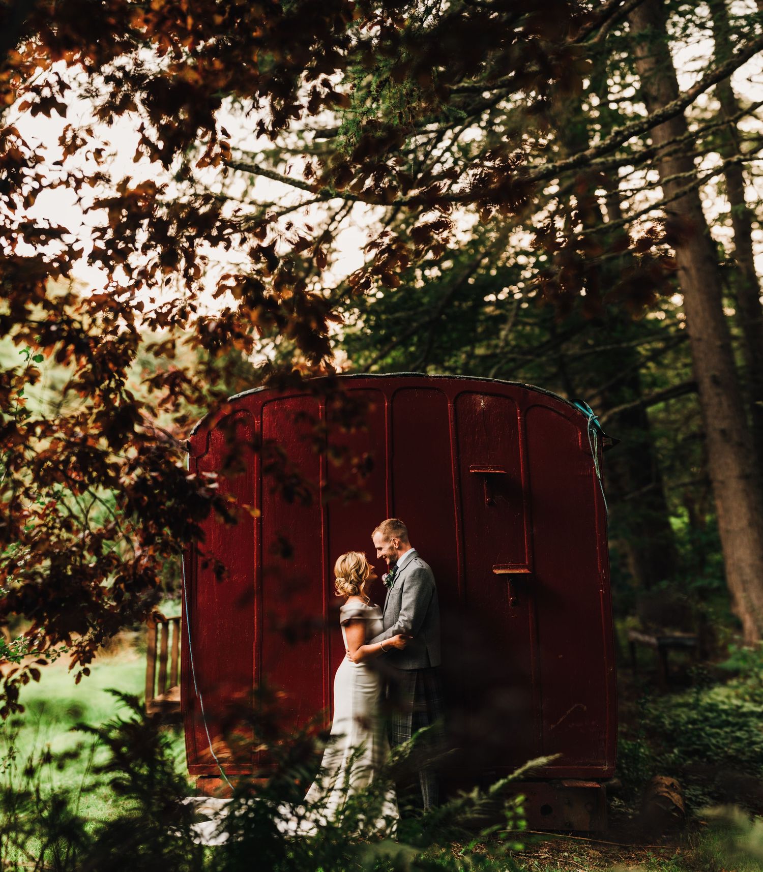 Romantic sunset photoshoot with rustic red vintage trailer backdrop in a wooded setting.