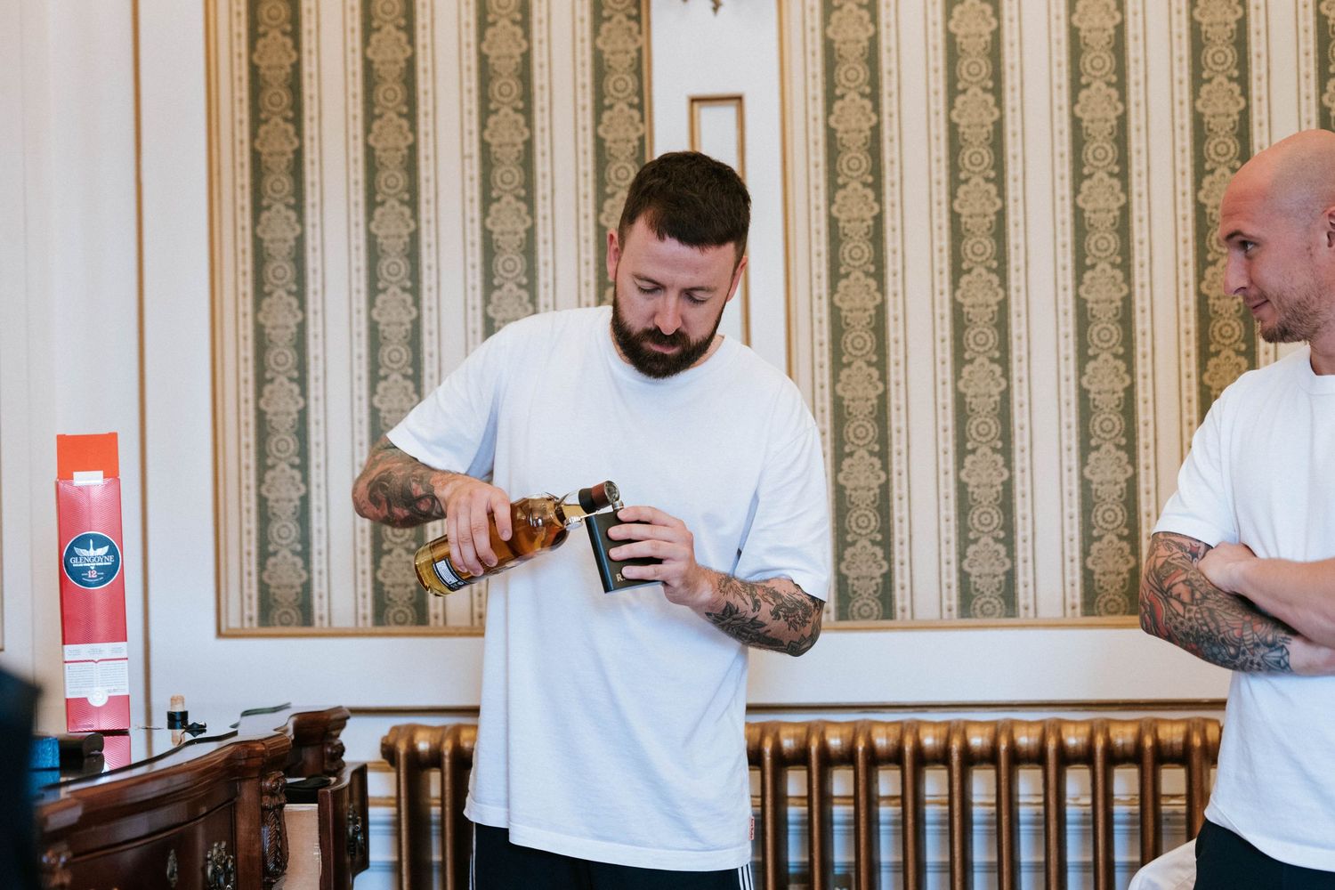 Groomsmen in white shirts sharing drinks and having fun during pre-wedding preparations.