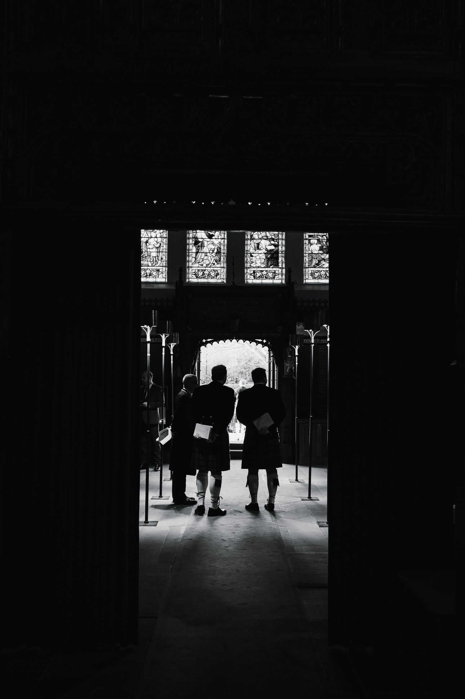 Silhouetted figures in a dark church doorway with illuminated stained glass above.